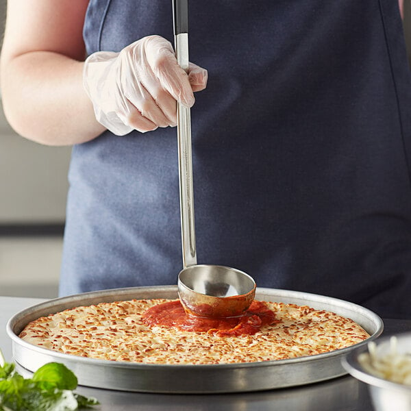 A person using a Vollrath stainless steel ladle to prepare a pizza.