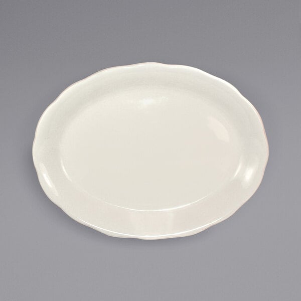 An International Tableware ivory stoneware platter with scalloped edges on a gray surface.