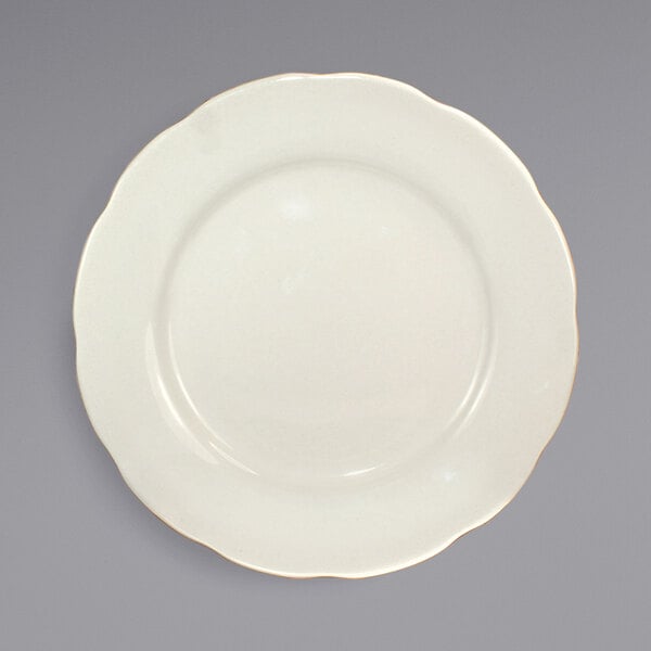 An International Tableware Victoria stoneware plate with a scalloped edge and gold trim.