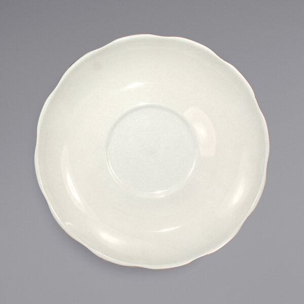 A white International Tableware scalloped edge saucer on a white surface.
