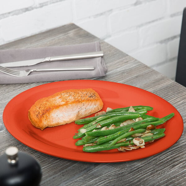 A red oval melamine platter with a piece of salmon and green beans.