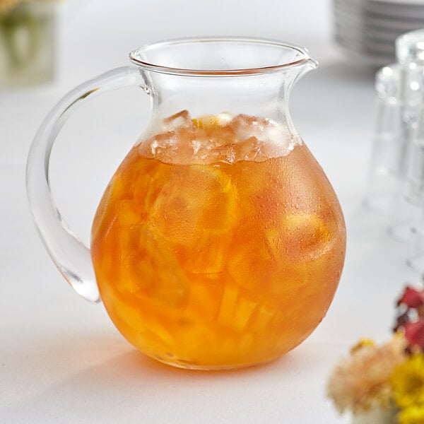 An Acopa fishbowl glass pitcher filled with orange liquid on a table.