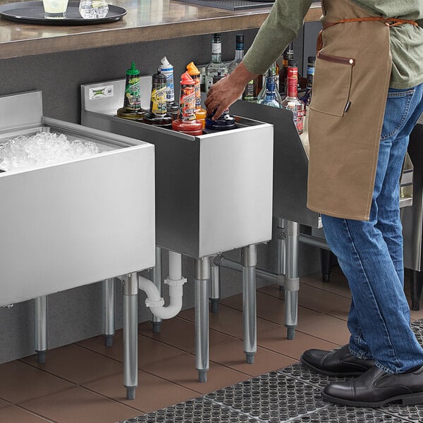 A man standing at a Regency stainless steel underbar ice bin with bottle holders.