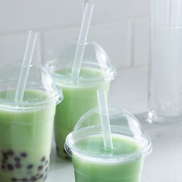 A group of green drinks with Choice translucent pointed straws on a white counter.