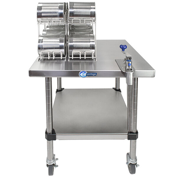 An Edlund mobile stainless steel table with a Edlund manual can opener on it with several cans on top.