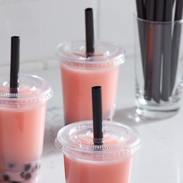 A plastic cup with a pink drink and a black unwrapped straw in it.