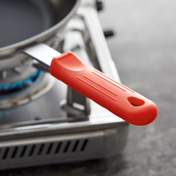 A close-up of a red Choice silicone pan handle sleeve on a pan sitting on a stove.