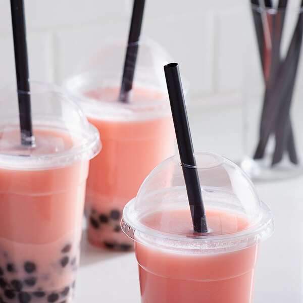 A group of pink drinks in plastic cups with black straws.