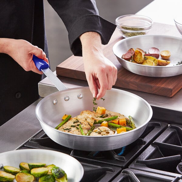 A person cooking brussels sprouts in a Choice aluminum fry pan with a blue silicone handle.