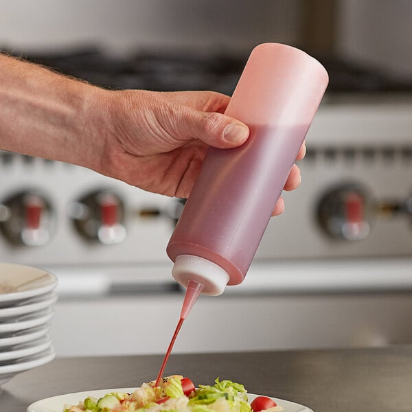 A hand holding a Server clear squeeze bottle of pink sauce over a plate of food.