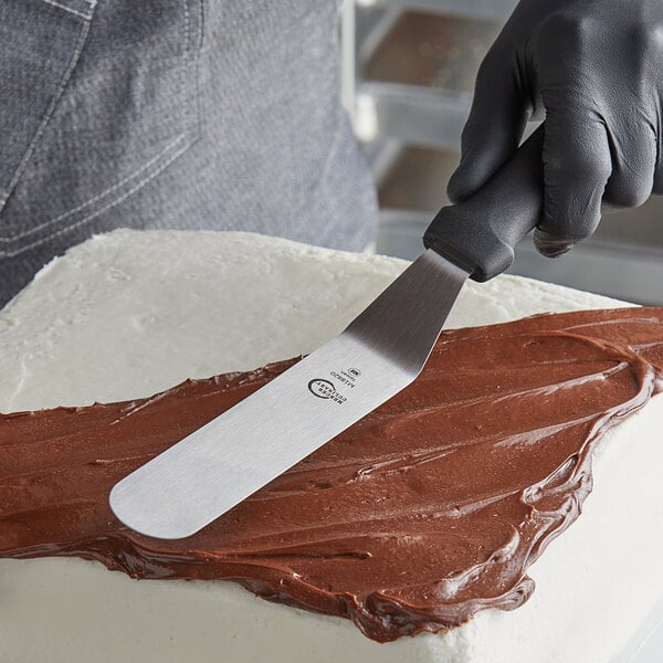 A person using a Mercer Culinary offset spatula to cut a cake.