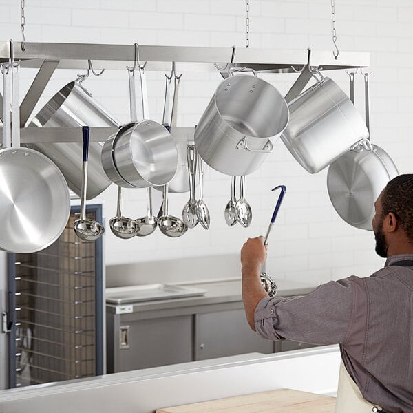A man in a kitchen with pots and pans hanging from a Regency stainless steel ceiling-mounted pot rack.