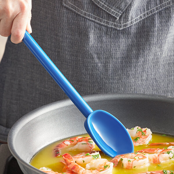 A person cooking shrimp in a pan with a blue Mercer Culinary Hell's Tools high temperature spoon.
