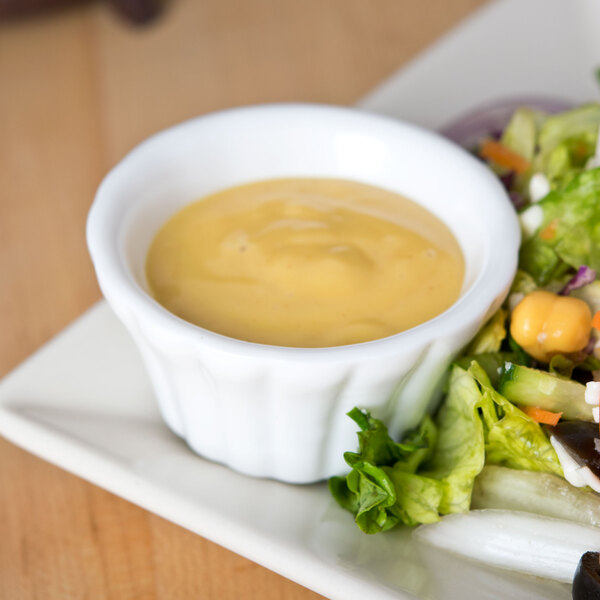 A plate of salad with a CAC Bone White floral ramekin of yellow sauce on the table.