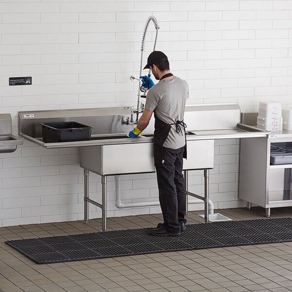 A man standing in a kitchen washing a Regency 2 compartment sink.