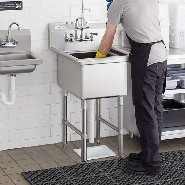A man washing a Regency stainless steel commercial sink in a professional kitchen.
