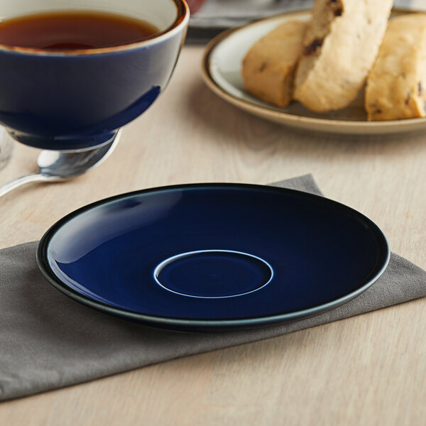 An Acopa Azora Blue stoneware saucer with a cup of tea on a table.