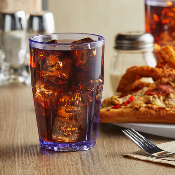 A blue plastic tumbler filled with ice tea on a table with a pizza.