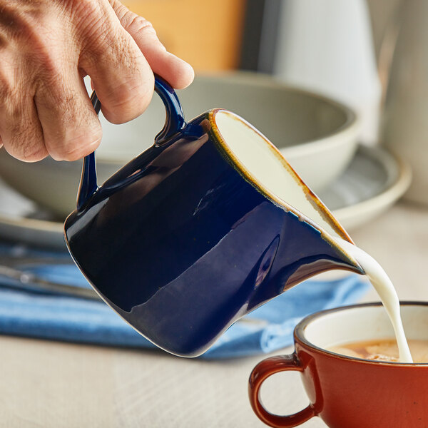 A person pouring milk into a blue pitcher.