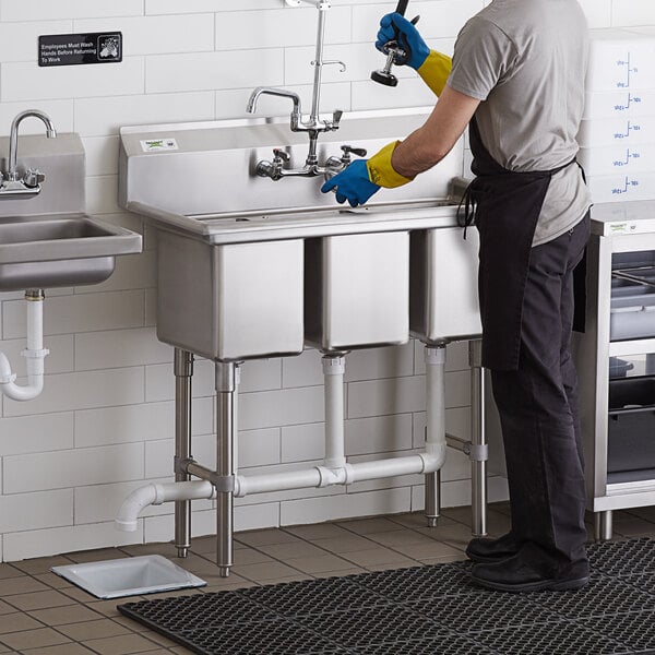 A man wearing gloves and gloves working at a Regency three compartment sink.