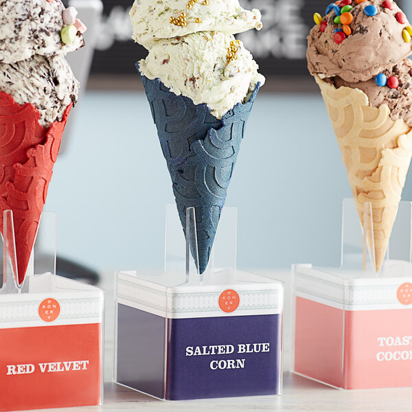 A Konery Salted Blue Corn waffle cone stand holding ice cream cones in a row, including a blue cone with white ice cream.