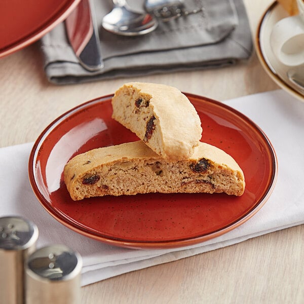 An Acopa Sedona Orange stoneware coupe plate with two pieces of biscotti on it.