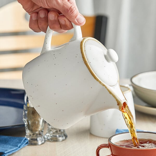A person pouring tea into a white Acopa Keystone stoneware teapot.