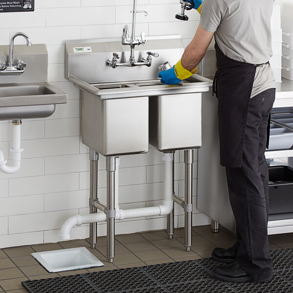 A man wearing a black apron and gloves using a Regency 2 compartment sink in a professional kitchen.