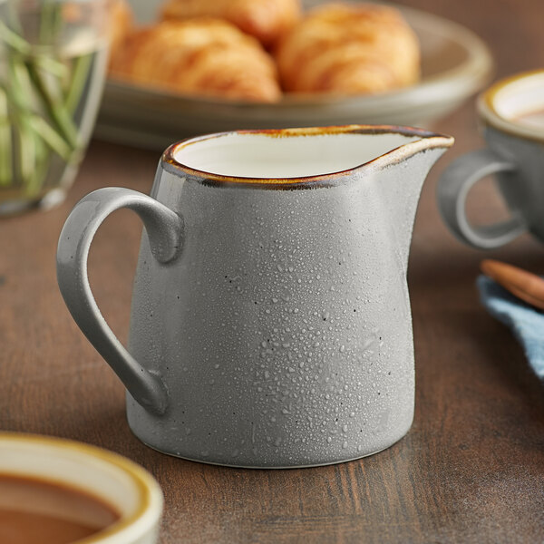 A Granite Gray Acopa Keystone stoneware creamer on a table with a cup of coffee.