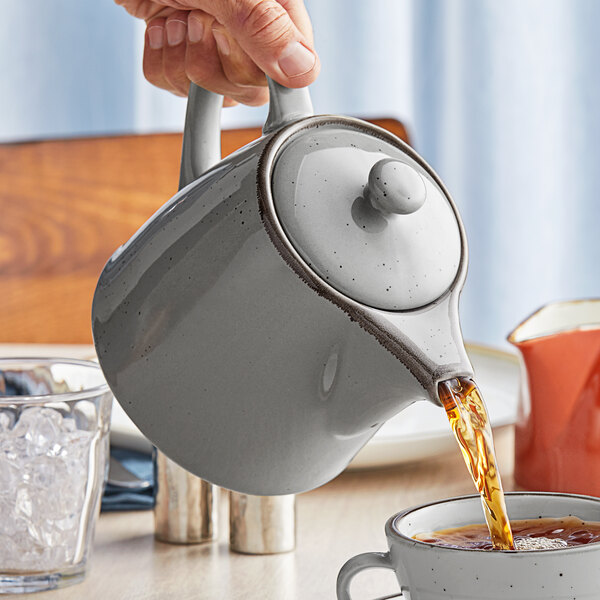 A person pouring tea into an Acopa Granite Gray stoneware teapot.