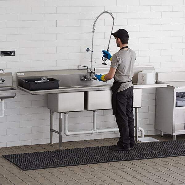 A man wearing an apron washing a Regency 3 compartment commercial sink.