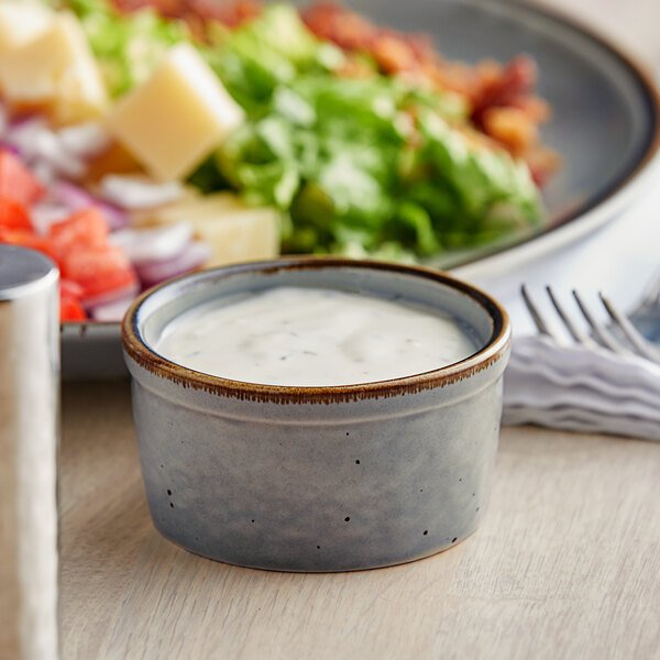 A bowl of Acopa Keystone granite gray stoneware filled with dressing on a table.