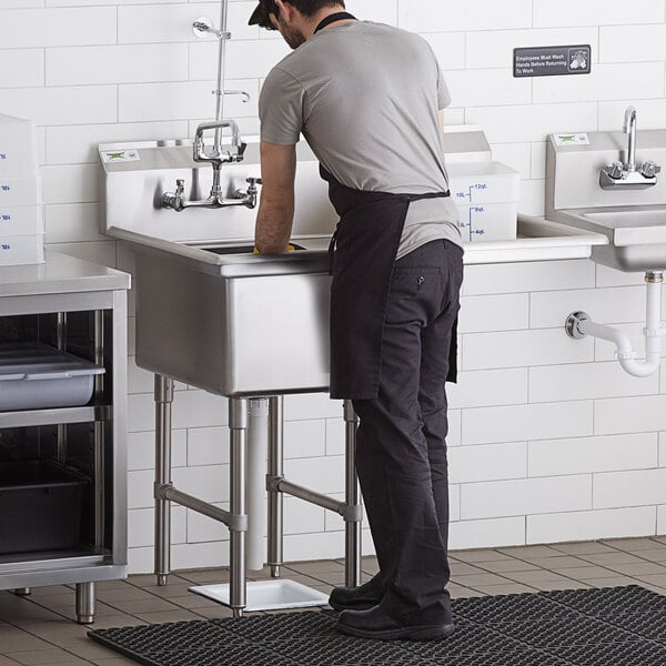A man washing dishes in a Regency stainless steel one compartment sink with right drainboard.