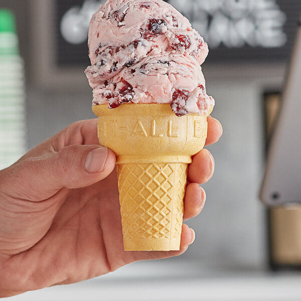 A hand holding a Keebler Eat-It-All cake cone with red and white topping.