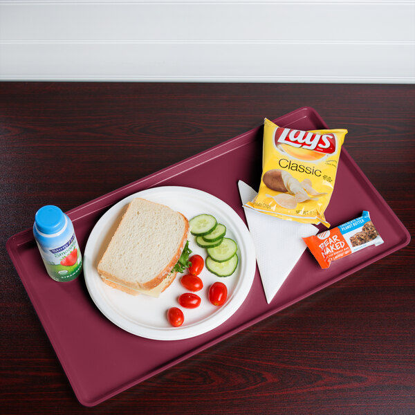 A Cambro cherry red dietary tray with a sandwich, chips, and a drink on it.