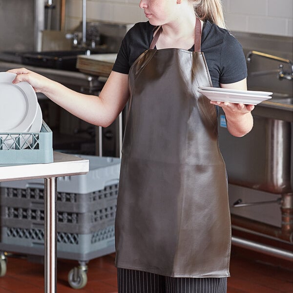 A woman wearing a San Jamar brown vinyl apron holding plates.