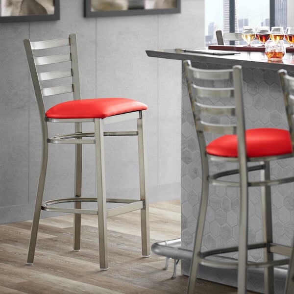A Lancaster Table & Seating clear coat finish ladder back bar stool with a red vinyl padded seat.