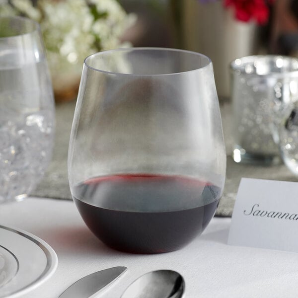 A Visions clear plastic stemless wine glass on a table next to a glass of red wine.