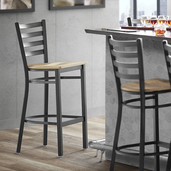 A Lancaster Table & Seating black metal ladder back bar stool with a driftwood seat.