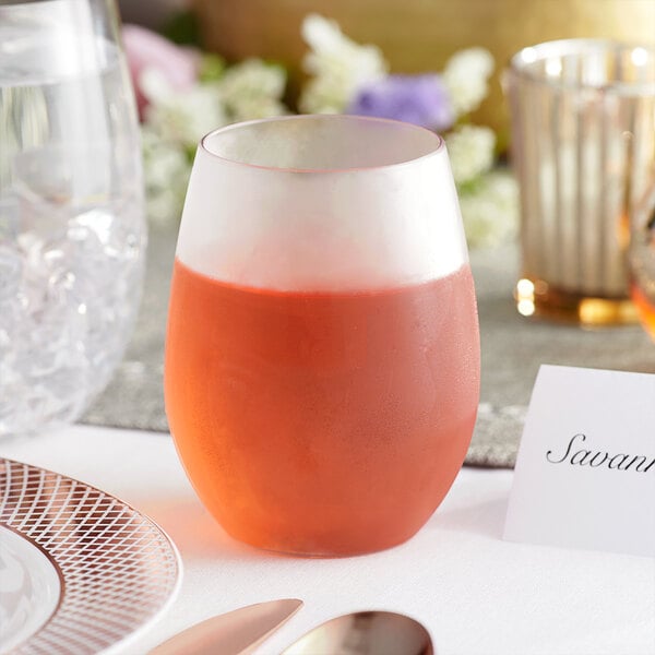 A Visions clear plastic stemless wine glass filled with a drink on a table.