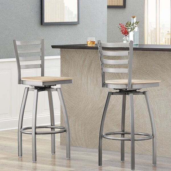 Two Lancaster Table & Seating ladder back swivel bar stools with natural wood seats at a counter.