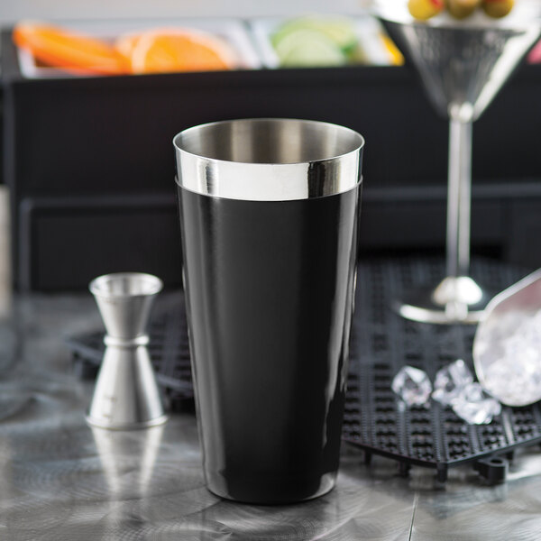 A black stainless steel cocktail shaker tin with a silver rim on a counter.