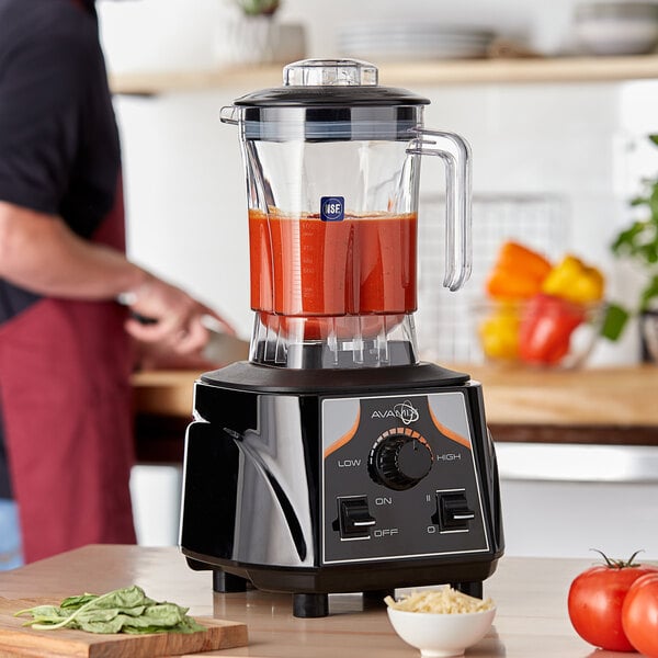 An AvaMix commercial blender filled with red tomato sauce on a wood floor.