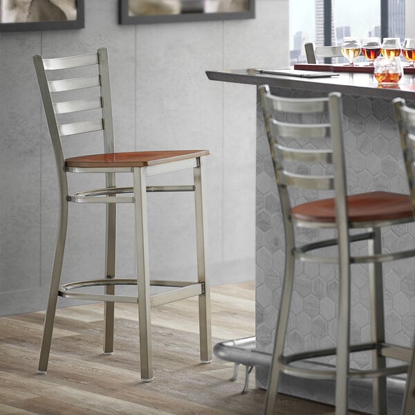 A Lancaster Table & Seating bar stool with a wooden ladder back and brown wood seat.
