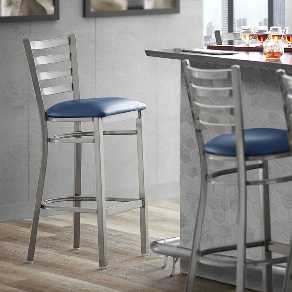 A Lancaster Table & Seating ladder back bar stool with navy blue vinyl padded seat.