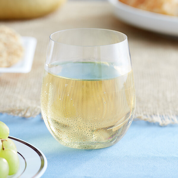 A Choice clear plastic stemless wine glass filled with white wine next to a plate of grapes.