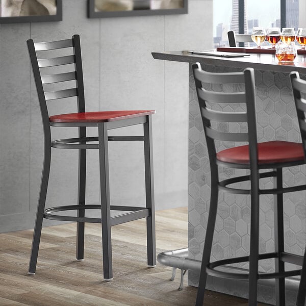 A Lancaster Table & Seating black finish ladder back bar stool with a mahogany wood seat.