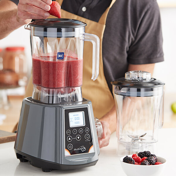 A man pouring strawberries into an AvaMix blender on a table with blackberries and raspberries.
