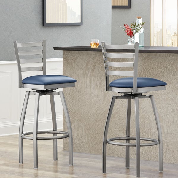 Two Lancaster Table & Seating ladder back swivel bar stools with navy vinyl padded seats at a counter.