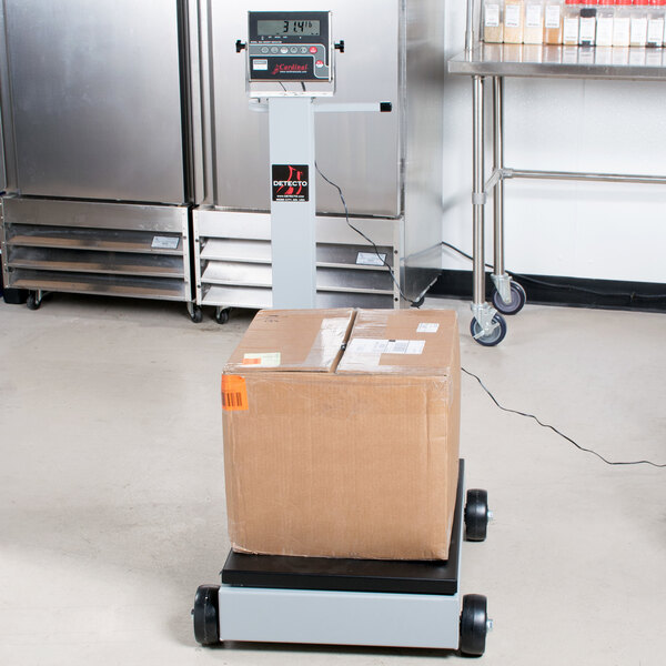 A brown box on a Cardinal Detecto portable digital floor scale with 185 indicator and tower display.